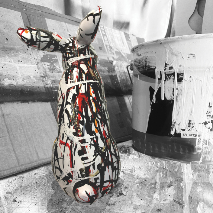 Sculpture de lapin Jean de Daphné Dejay dans l'atelier devant un pot de peinture qui coule