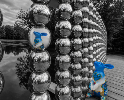Sculpture de lapin Jean de Daphné Dejay devant une installation de sphères réfléchissantes au bord de l'eau.