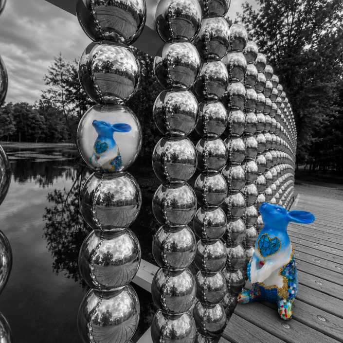 Sculpture de lapin Jean de Daphné Dejay devant une installation de sphères réfléchissantes au bord de l'eau.